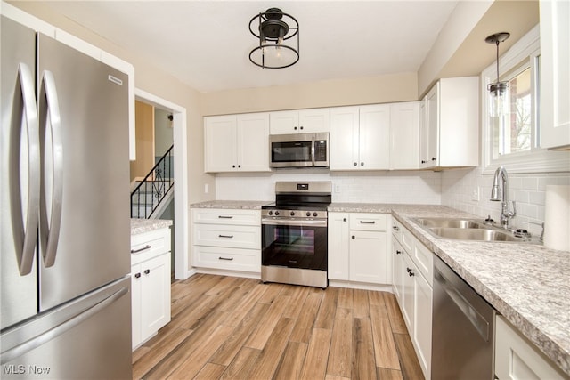 kitchen featuring pendant lighting, white cabinets, sink, light hardwood / wood-style flooring, and stainless steel appliances