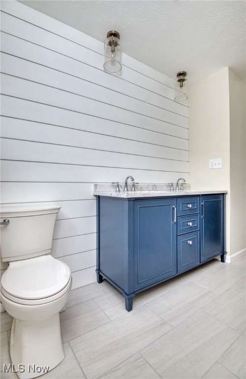 bathroom featuring wood walls, vanity, a textured ceiling, and toilet