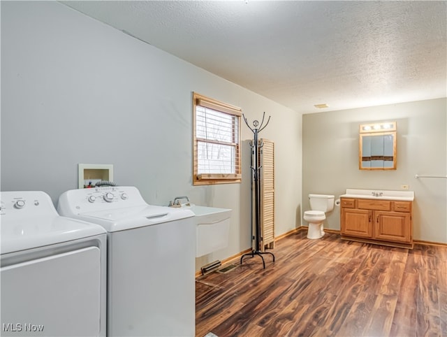 clothes washing area with sink, a textured ceiling, dark wood-type flooring, and washing machine and clothes dryer