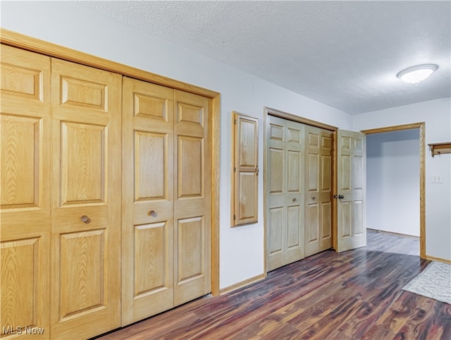 unfurnished bedroom with a textured ceiling, dark hardwood / wood-style flooring, and two closets