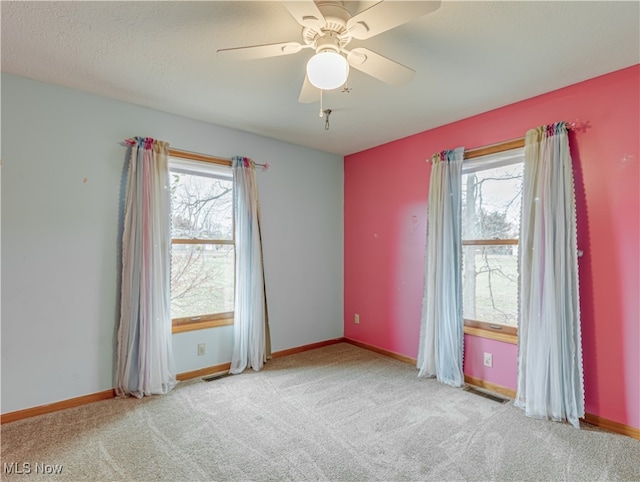 carpeted spare room featuring ceiling fan, a textured ceiling, and a wealth of natural light