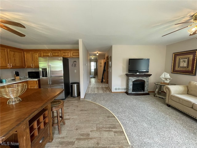 kitchen featuring ceiling fan, a stone fireplace, stainless steel fridge with ice dispenser, and light carpet