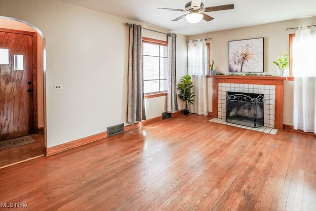 unfurnished living room featuring light hardwood / wood-style floors, ceiling fan, and a tiled fireplace