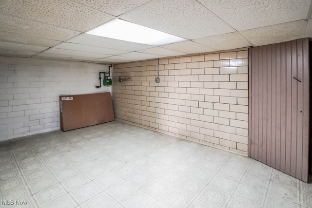 basement featuring wooden walls and a drop ceiling