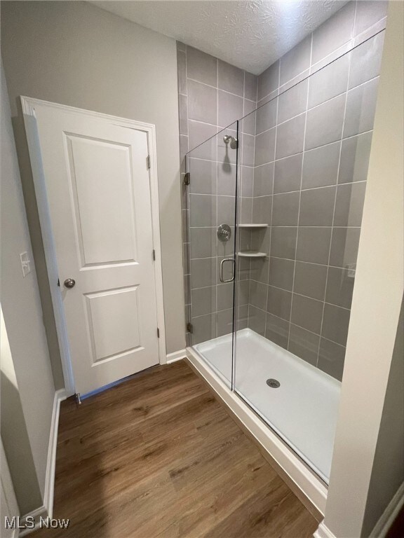 bathroom featuring a textured ceiling, hardwood / wood-style flooring, and a shower with door