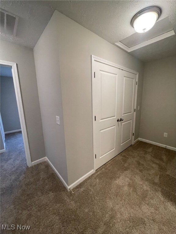 corridor with a textured ceiling and dark carpet