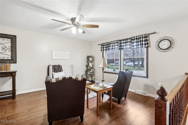 sitting room with a textured ceiling, ceiling fan, and dark wood-type flooring