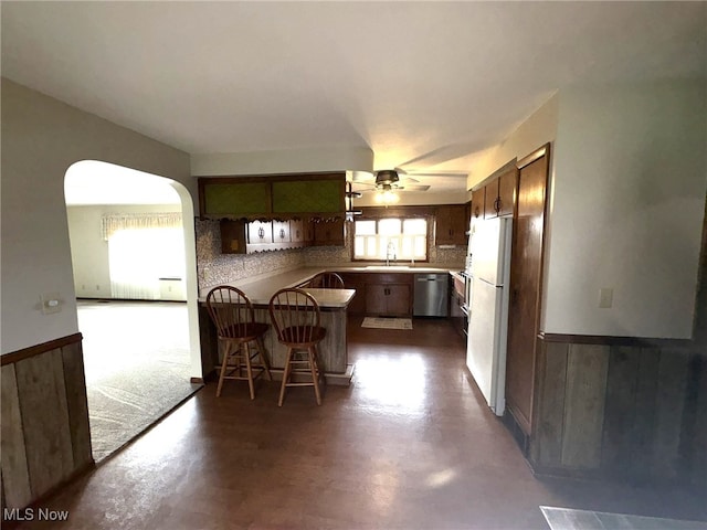 kitchen featuring ceiling fan, dishwasher, kitchen peninsula, white fridge, and a kitchen bar