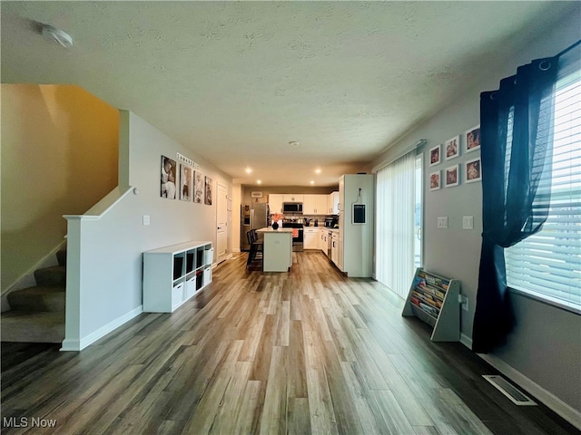 kitchen with a center island, white cabinets, a textured ceiling, appliances with stainless steel finishes, and light hardwood / wood-style floors