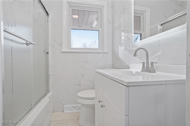 full bathroom featuring vanity, toilet, bath / shower combo with glass door, and tile walls