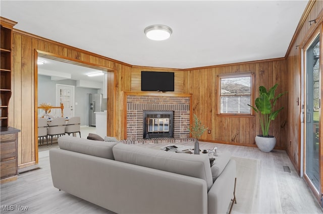 living room with light wood-type flooring, wooden walls, and a brick fireplace