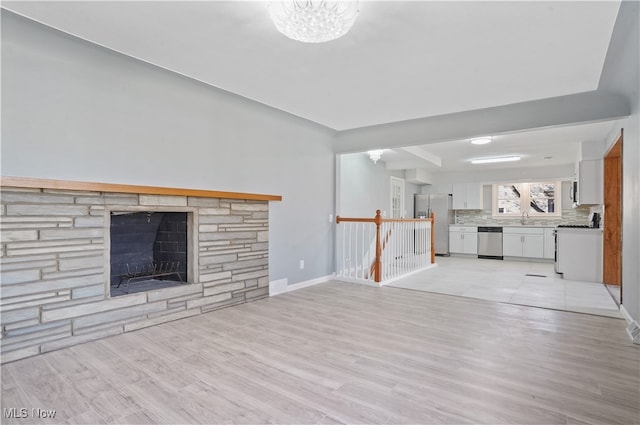 unfurnished living room featuring a stone fireplace, sink, light hardwood / wood-style floors, and an inviting chandelier