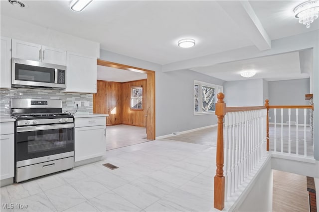 kitchen with white cabinets, tasteful backsplash, beamed ceiling, stainless steel appliances, and a chandelier