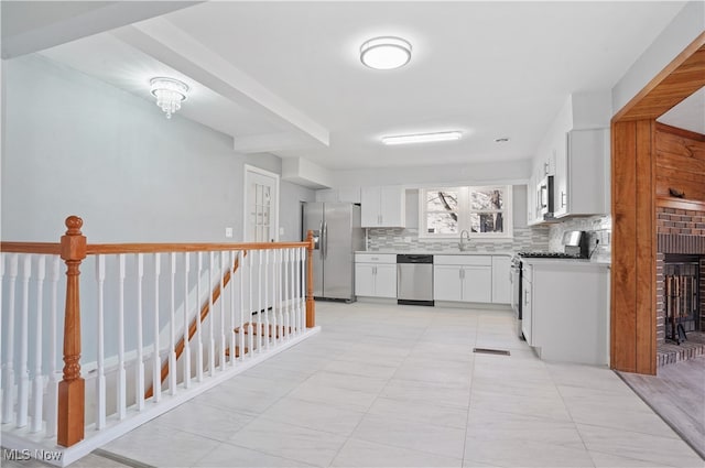 kitchen with decorative backsplash, appliances with stainless steel finishes, a brick fireplace, sink, and white cabinetry