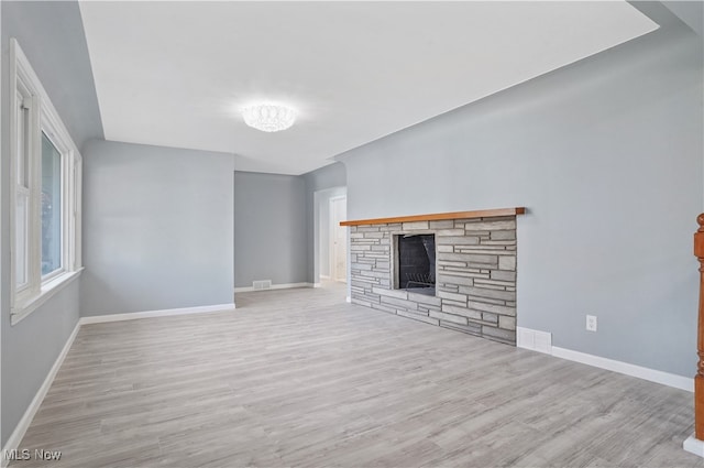 unfurnished living room featuring a stone fireplace and light hardwood / wood-style flooring