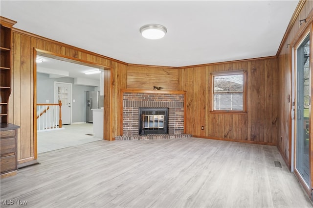 unfurnished living room featuring a fireplace, light hardwood / wood-style flooring, wooden walls, and crown molding