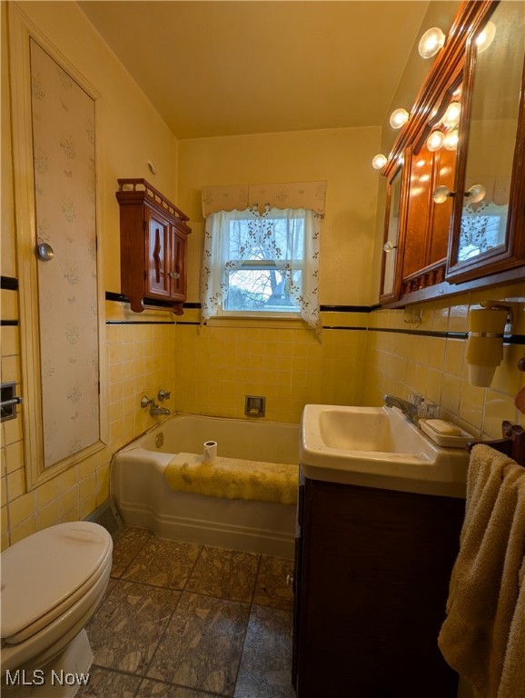 bathroom with a bath, vanity, toilet, and tile walls