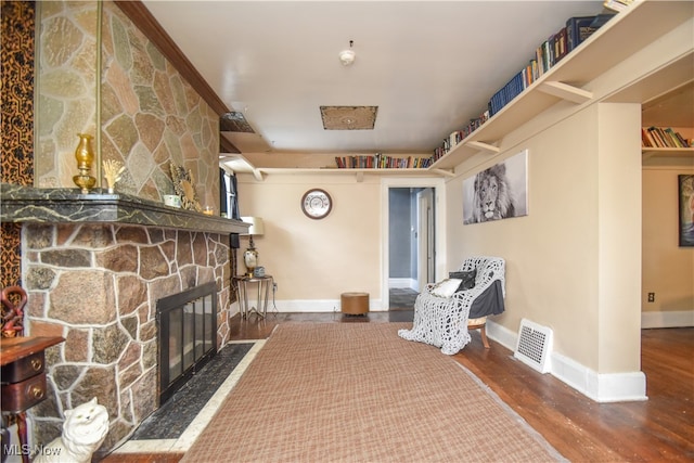 living area featuring a stone fireplace and dark wood-type flooring