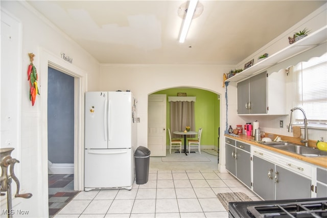 kitchen featuring crown molding, sink, light tile patterned floors, white refrigerator, and gray cabinets