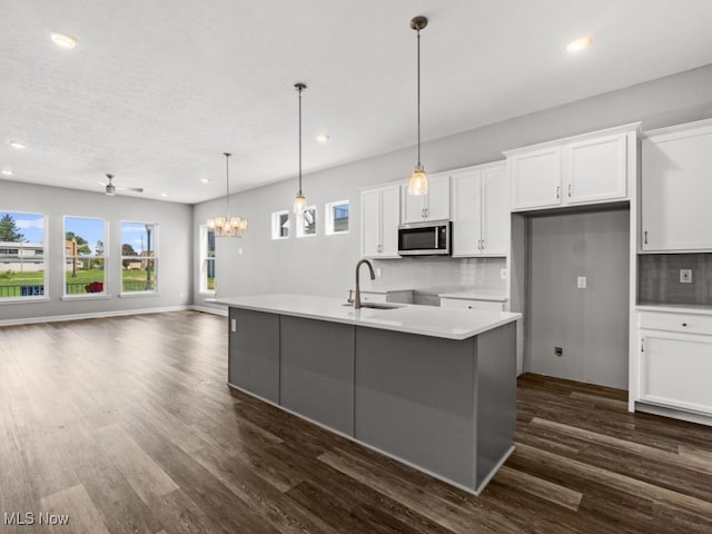 kitchen with a center island with sink, ceiling fan with notable chandelier, white cabinetry, and hanging light fixtures