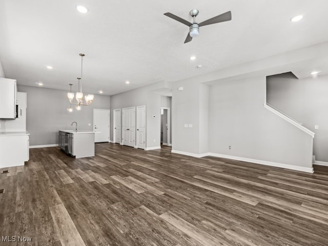 unfurnished living room featuring ceiling fan with notable chandelier, sink, and dark wood-type flooring