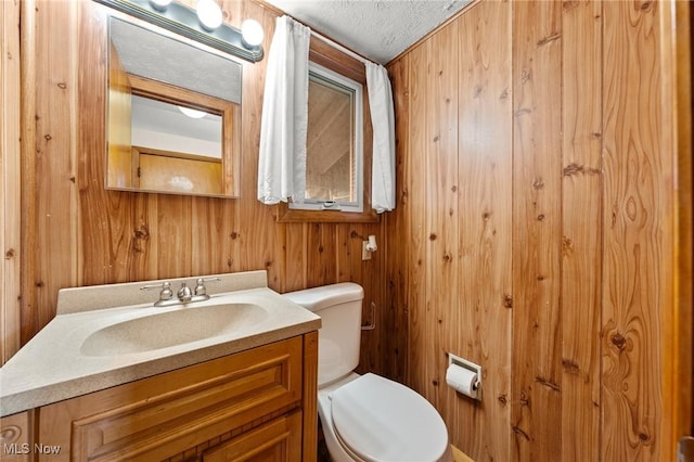 bathroom featuring vanity, toilet, a textured ceiling, and wooden walls