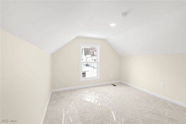 additional living space featuring light carpet, vaulted ceiling, and baseboards