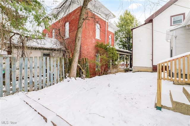 snow covered property featuring brick siding and fence