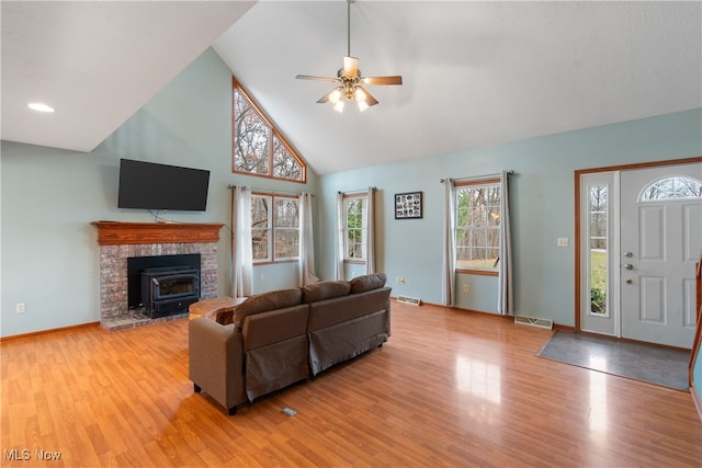 living room with ceiling fan, a wood stove, high vaulted ceiling, and light hardwood / wood-style flooring