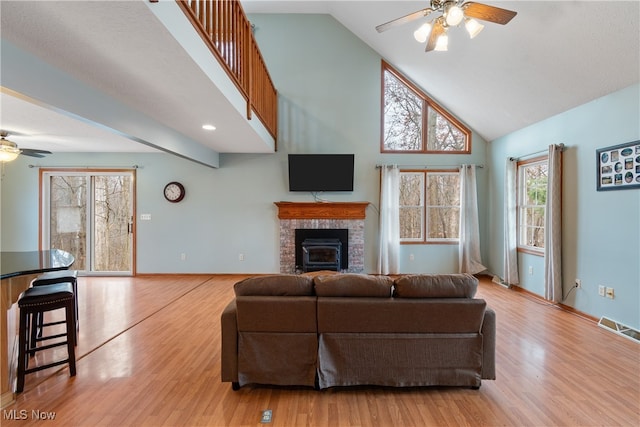 living room with a wood stove, high vaulted ceiling, light hardwood / wood-style flooring, and ceiling fan