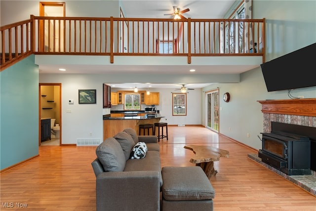 living room with ceiling fan, a wood stove, and light hardwood / wood-style flooring