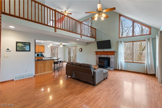 living room with a wood stove, ceiling fan, light hardwood / wood-style flooring, and high vaulted ceiling