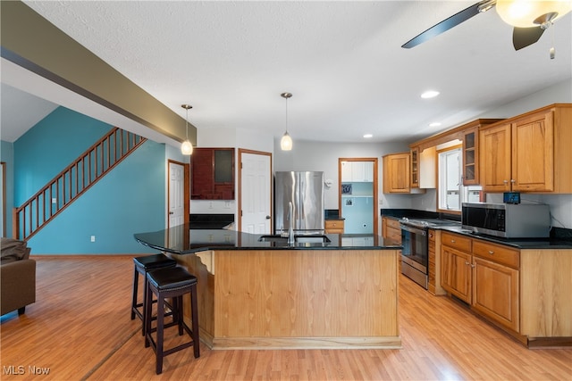 kitchen featuring sink, an island with sink, appliances with stainless steel finishes, and light hardwood / wood-style flooring