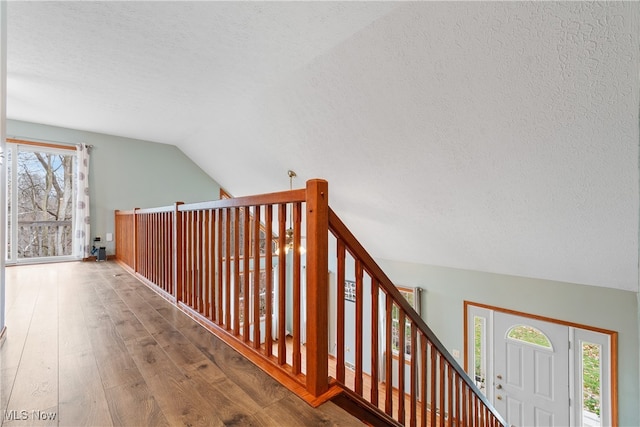 hall featuring hardwood / wood-style flooring, lofted ceiling, and a textured ceiling