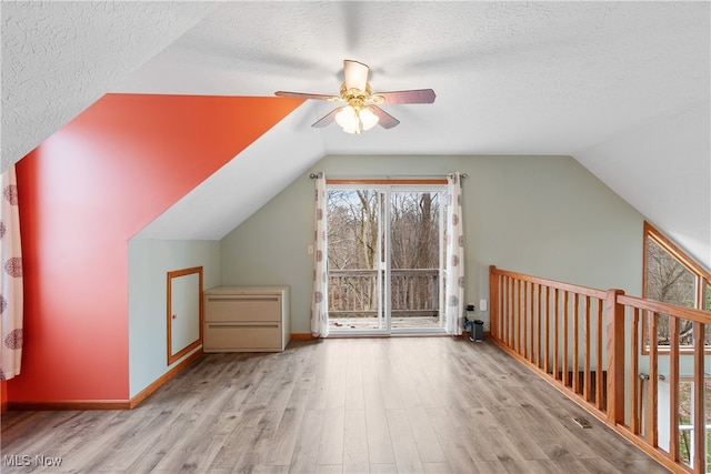 additional living space featuring ceiling fan, lofted ceiling, a textured ceiling, and light hardwood / wood-style flooring