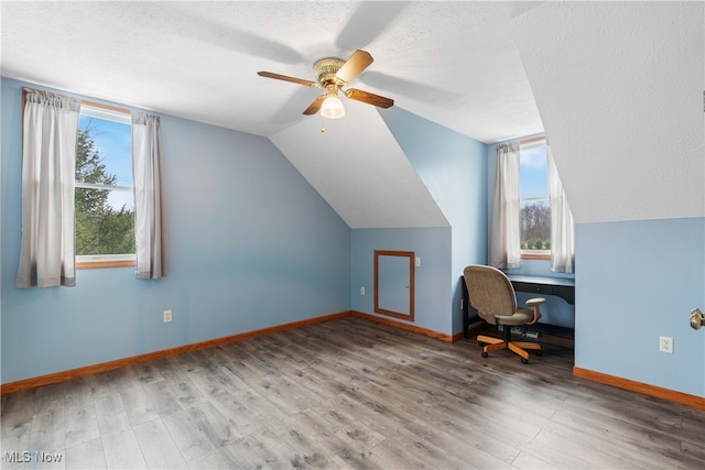 additional living space featuring a textured ceiling, ceiling fan, wood-type flooring, built in desk, and lofted ceiling