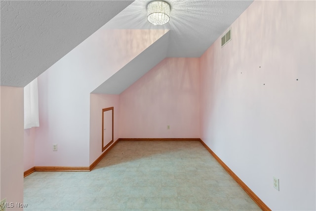 bonus room with a chandelier, a textured ceiling, and vaulted ceiling