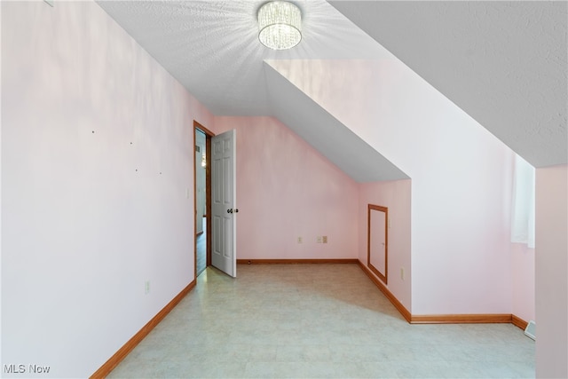 additional living space featuring a chandelier, a textured ceiling, and vaulted ceiling