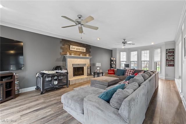 living room with a tile fireplace, light hardwood / wood-style floors, ceiling fan, and crown molding