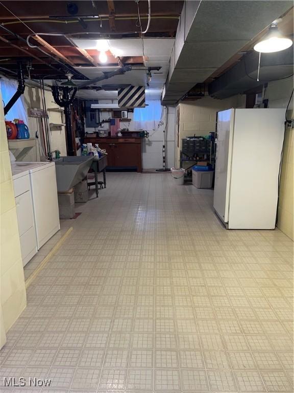 basement featuring white refrigerator, separate washer and dryer, and sink