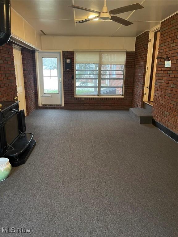 unfurnished living room featuring carpet flooring, a wood stove, and brick wall