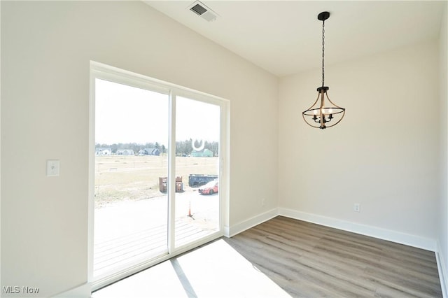spare room featuring wood finished floors, a chandelier, and baseboards