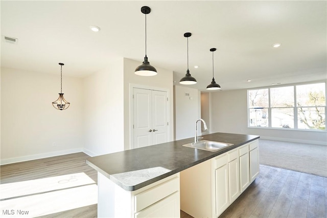 kitchen featuring a sink, open floor plan, light wood-style floors, a kitchen island with sink, and baseboards
