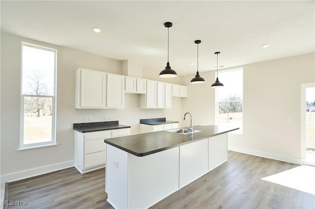 kitchen featuring a sink, white cabinetry, wood finished floors, a kitchen island with sink, and baseboards