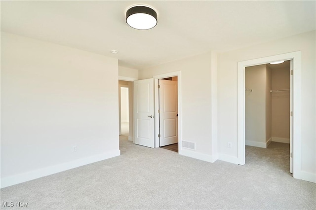 unfurnished bedroom featuring carpet floors, a walk in closet, and baseboards