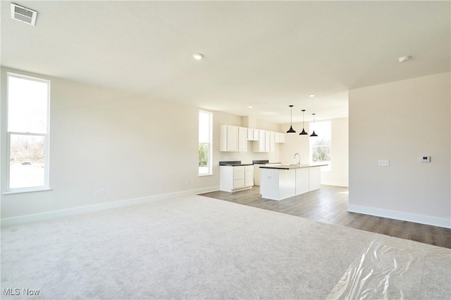 unfurnished living room with baseboards, plenty of natural light, light colored carpet, a sink, and recessed lighting