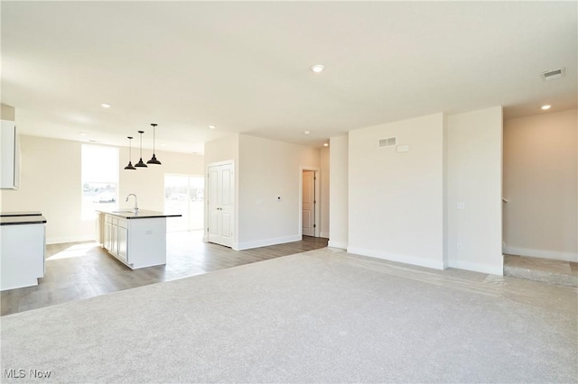unfurnished living room featuring a sink, recessed lighting, light colored carpet, and baseboards