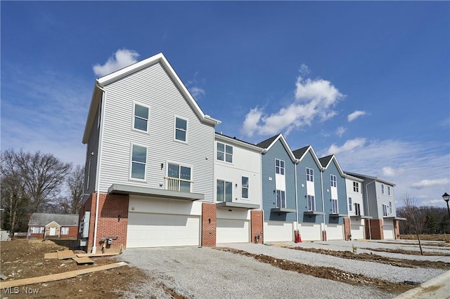 townhome / multi-family property featuring brick siding, driveway, a garage, and a residential view