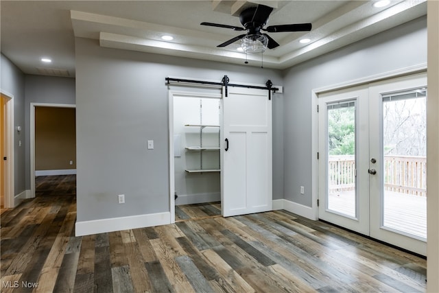 unfurnished bedroom featuring french doors, access to outside, ceiling fan, dark wood-type flooring, and a barn door