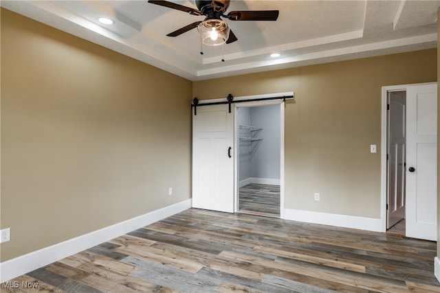 unfurnished bedroom featuring hardwood / wood-style floors, a barn door, a tray ceiling, and ceiling fan